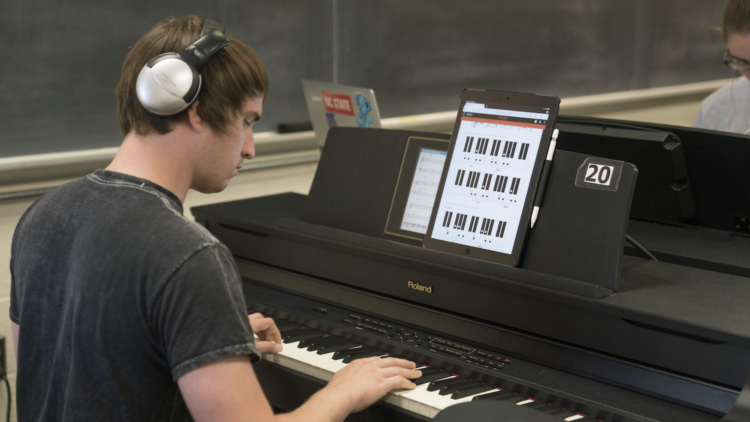 Lucas Sanders practices playing piano using the Piano+ interactive method book created through a DELTA Grant in partnership with Olga Kleiankina from the Department of Music. Photo by Erin Zanders. The student is playing piano and has a tablet in front of him with the Piano+ loaded on the screen.