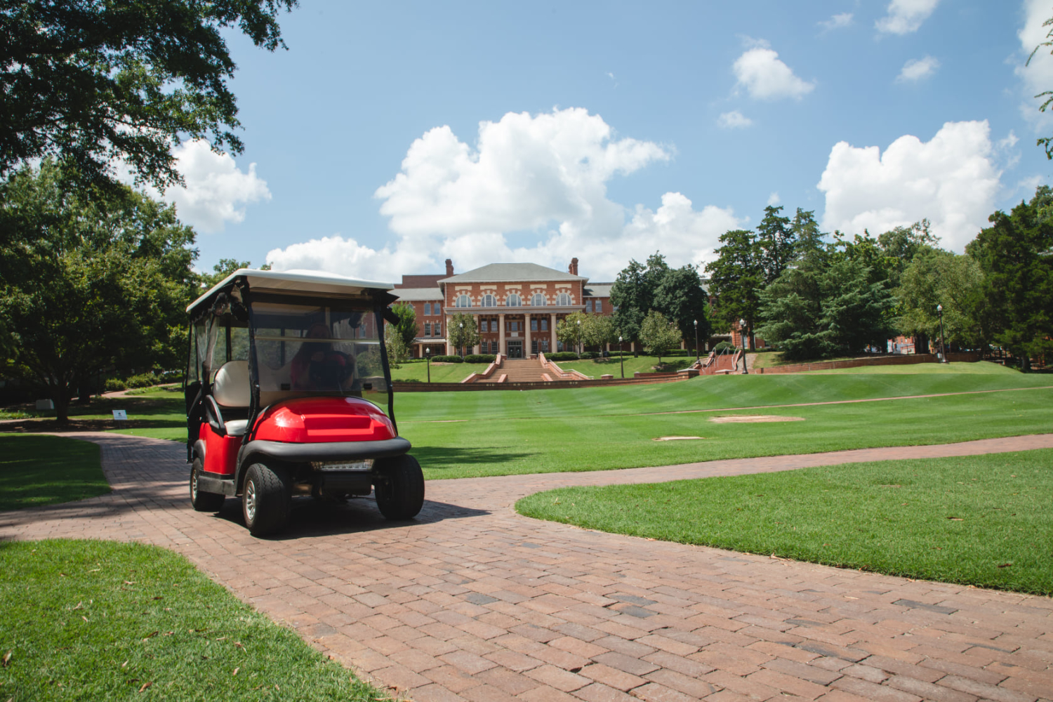 A red Wolfpack Pick Up golf cart drives along the brick path on the Court of Carolina