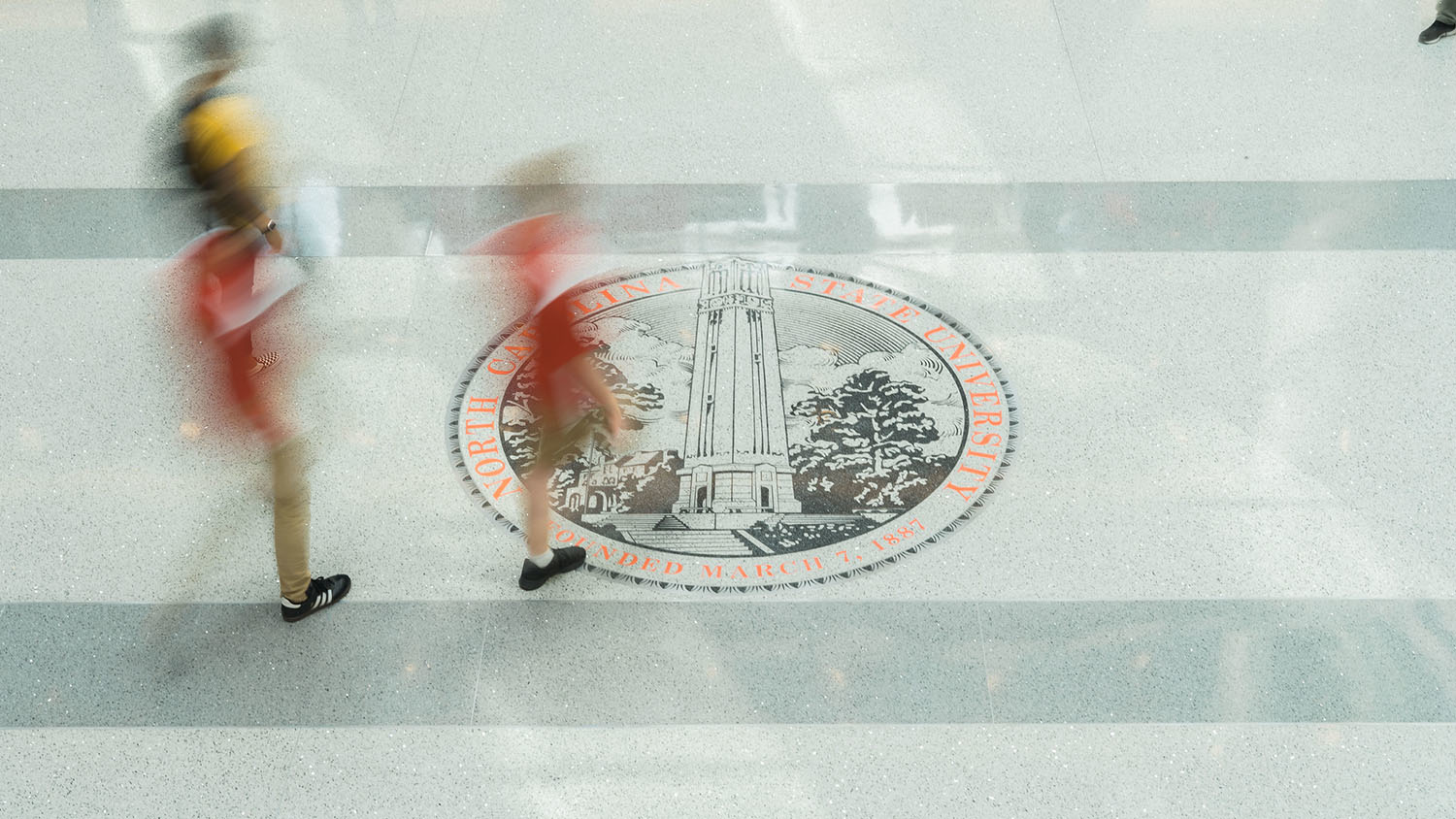 Students walk by the NC State seal in Talley Student Union
