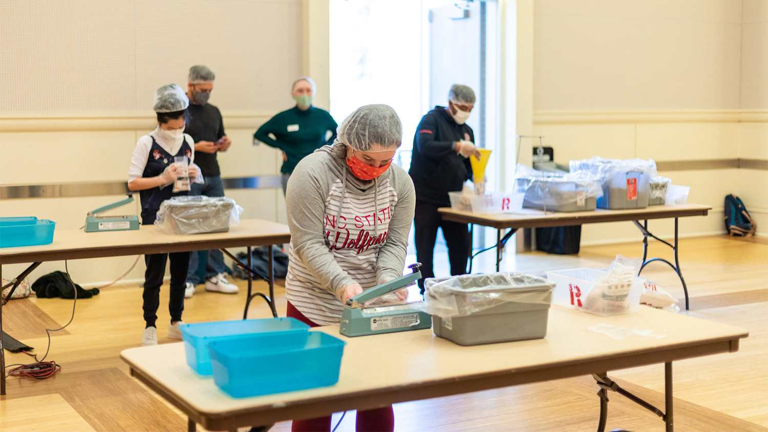 Students stand at tables and pack meals into boxes