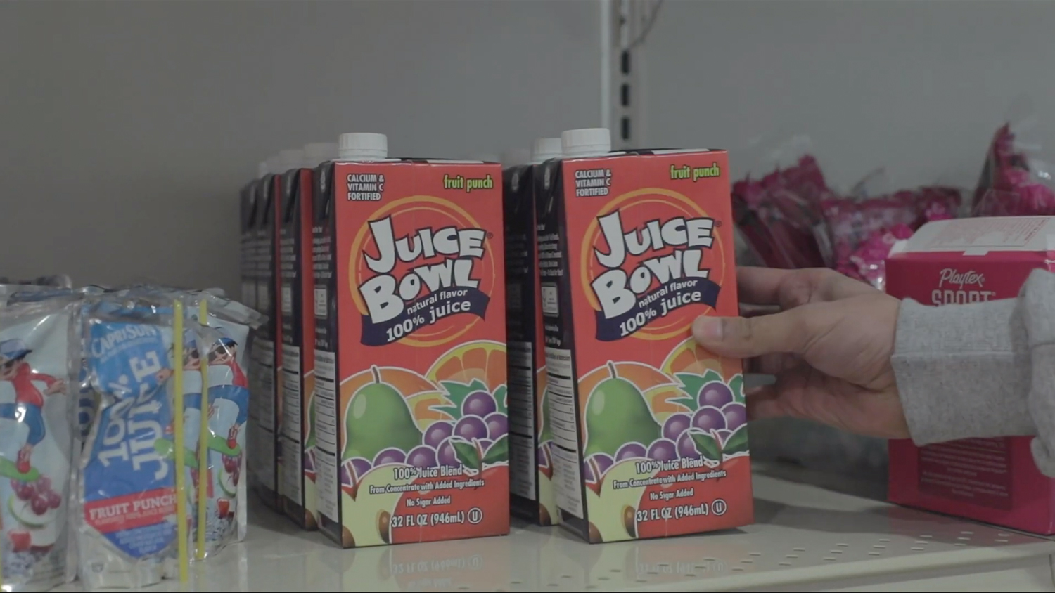A staff member's hand places a juice box on a shelf
