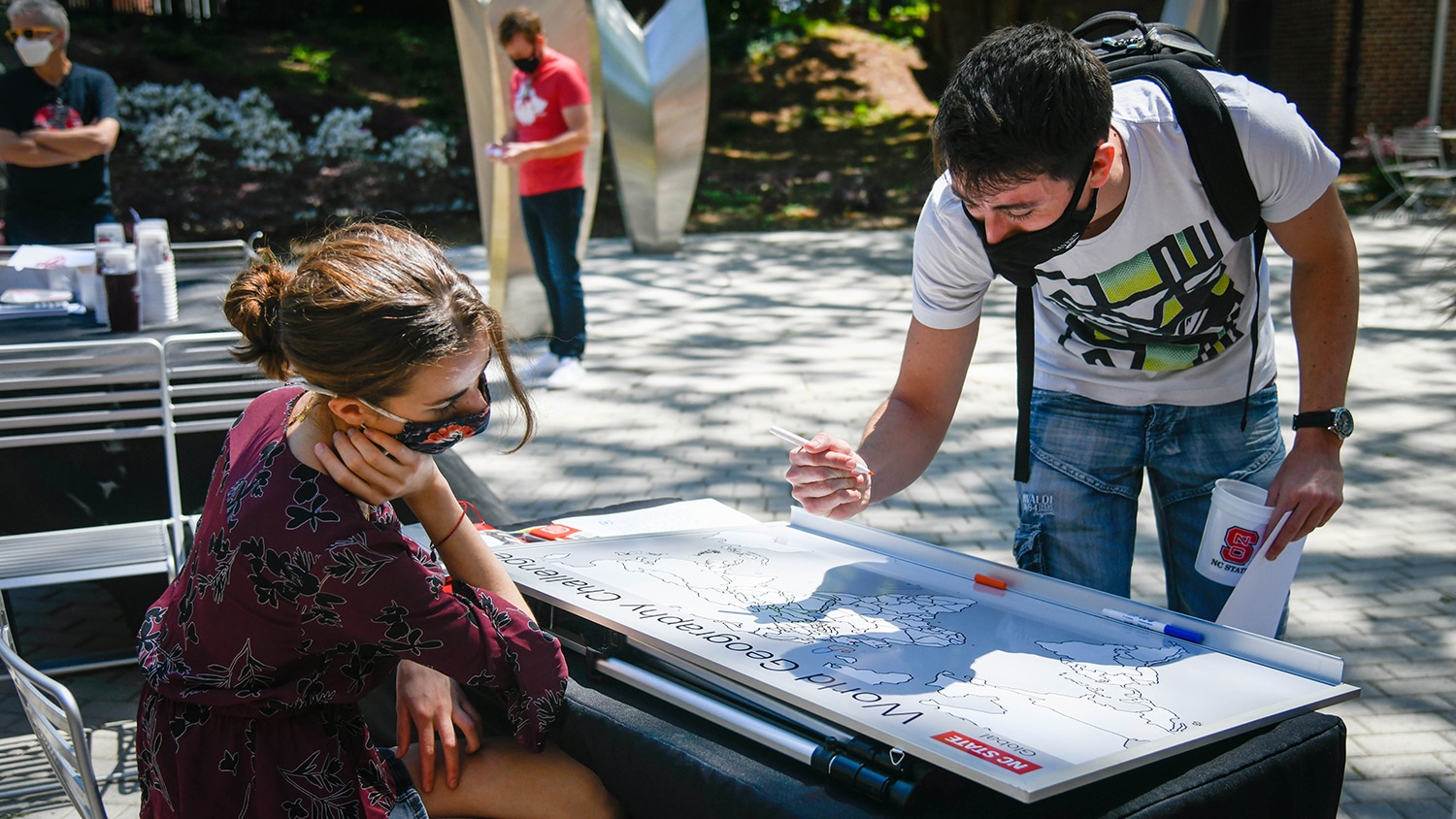 A male student marks his hometown on a map of the world as a female student looks on.
