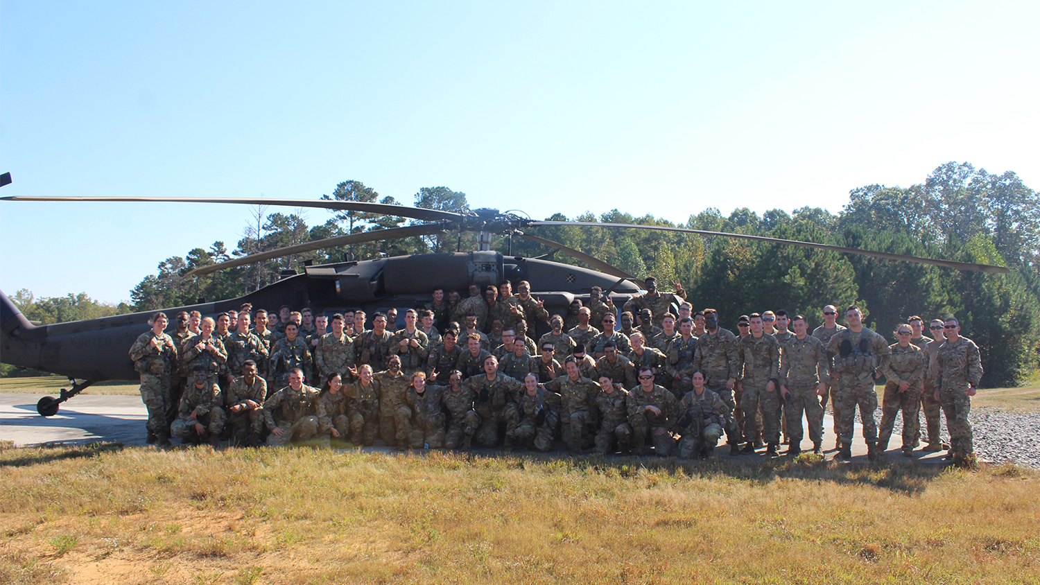 A group of cadets in uniform pose in front of a Blackhawk helicopter in an open field