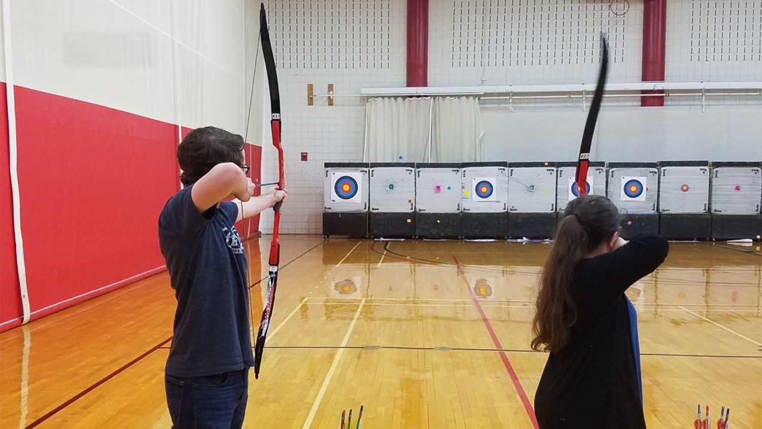 Students aim their bows at targets during an archery course