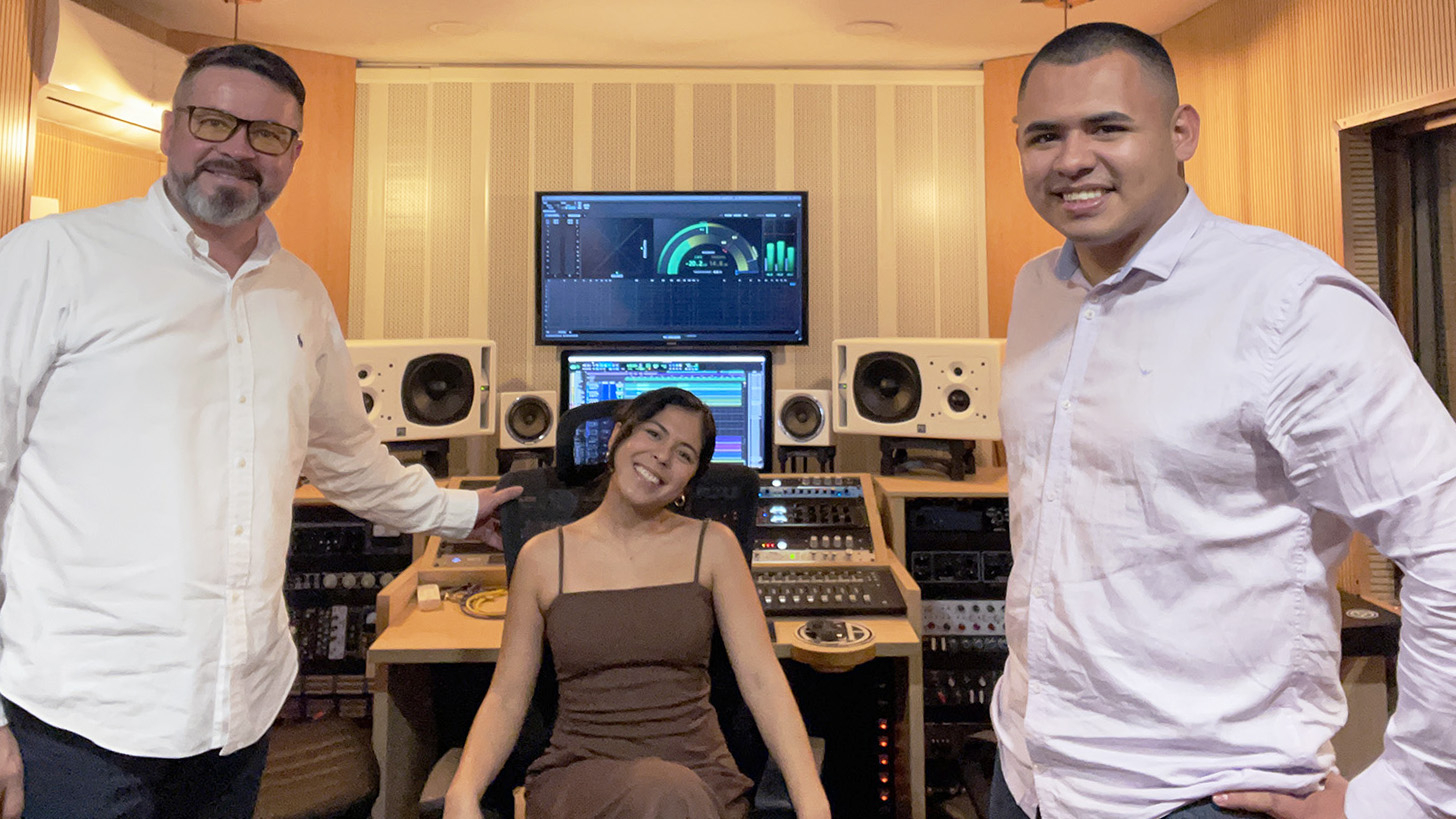 Daniela Gaudete sits between two producers in front of computer and recording equipment in a studio