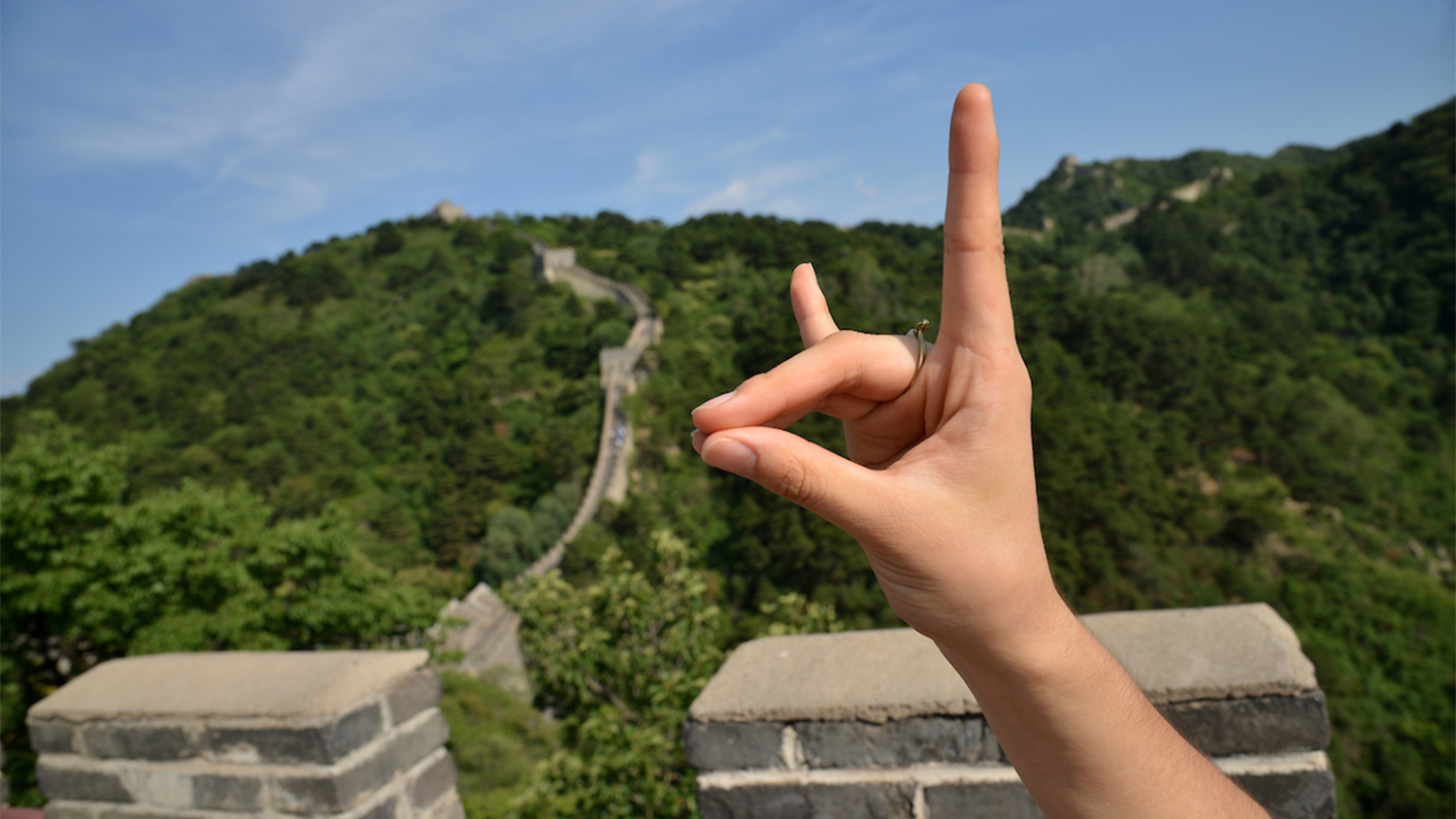A hand making a wolfie sign in front of the Great Wall of China