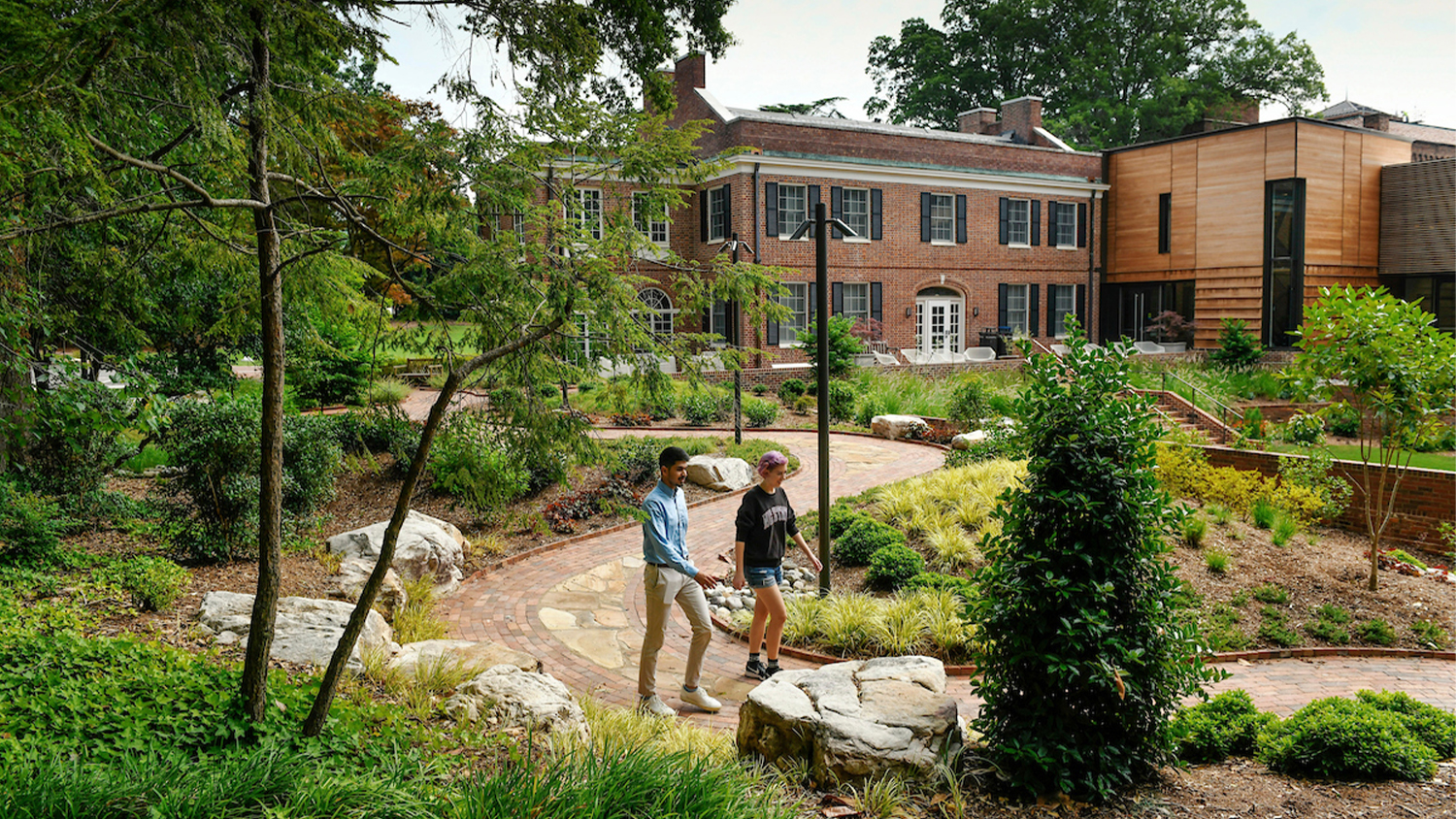 Two people walk through the gardens outside of the Gregg Museum
