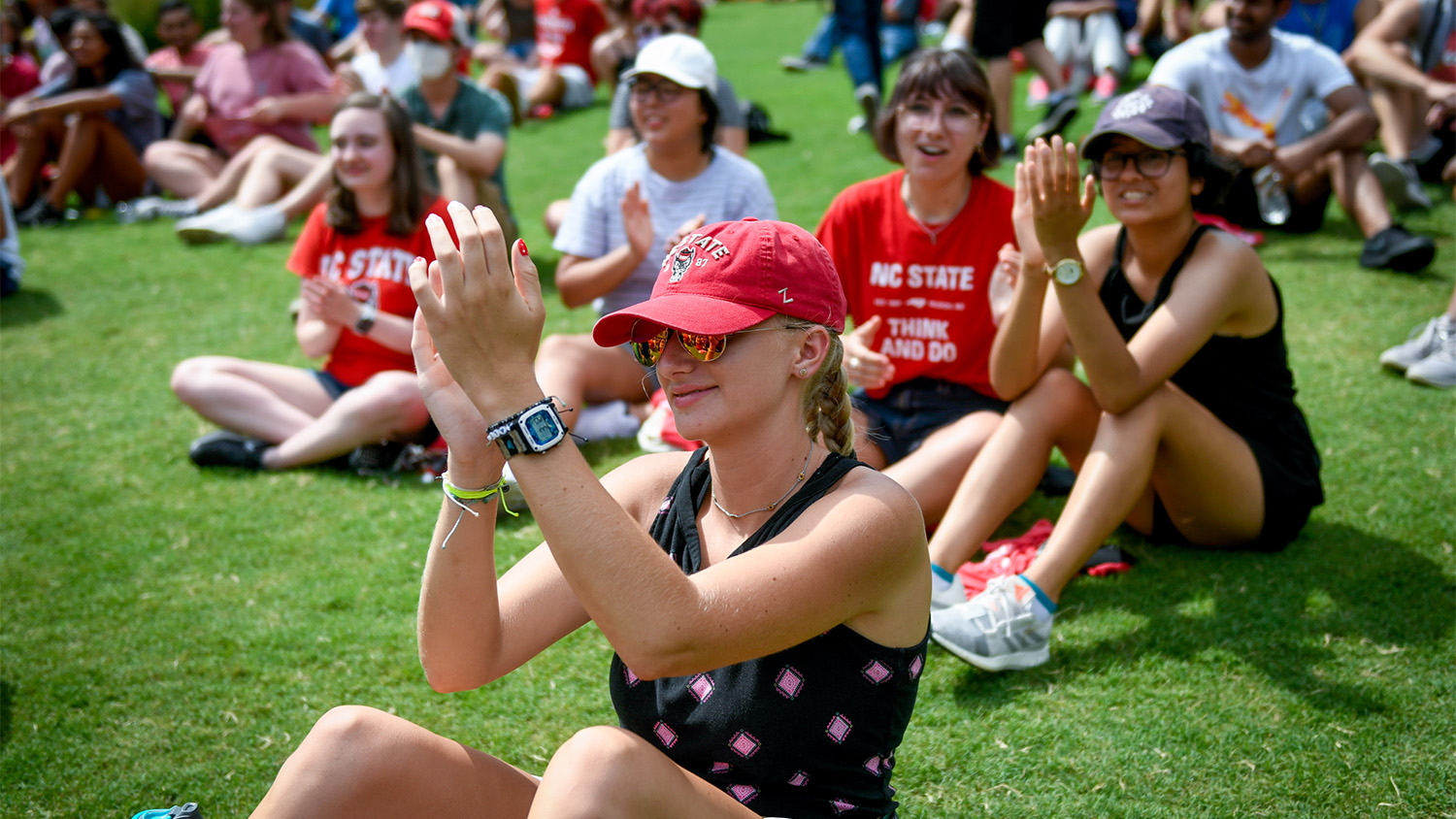 A student attending outdoor Convocation in 2021 claps along as the band plays the school fight song