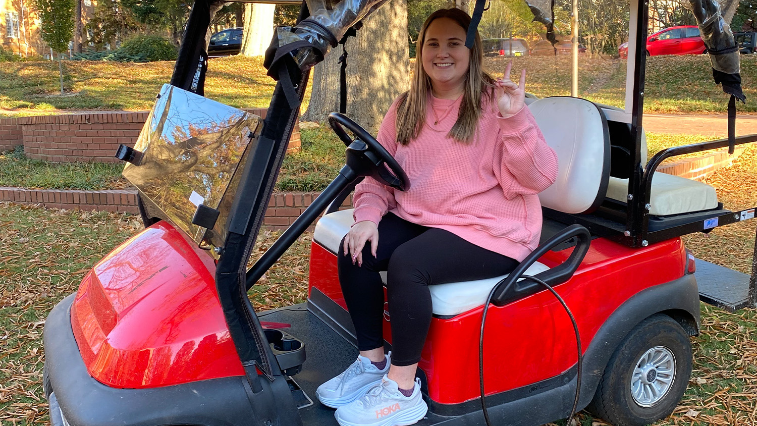 Brock Derrow sitting in the driver's seat of a red golf cart and making a wolfie sign with her hand