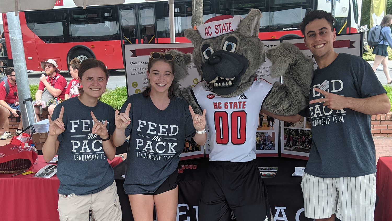 Mr Wuf poses with three members of the Feed the Pack food pantry team in front of a table at Packapalooza
