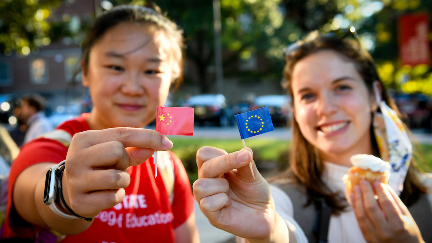Two female students hold up miniature flags representing their home countries