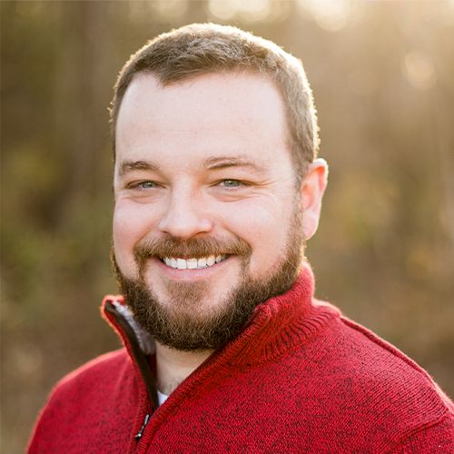 Headshot of Joshua Reaves outside in a red sweater.